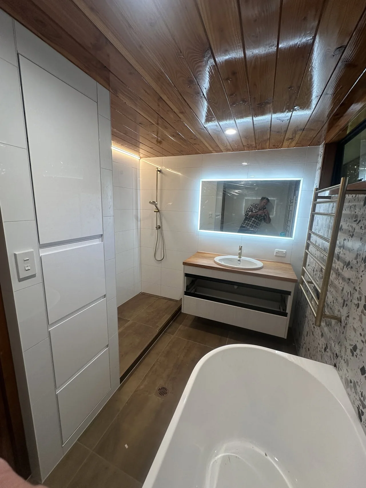 Bathroom with freestanding bath, illuminated mirror, stone wall and timber ceiling