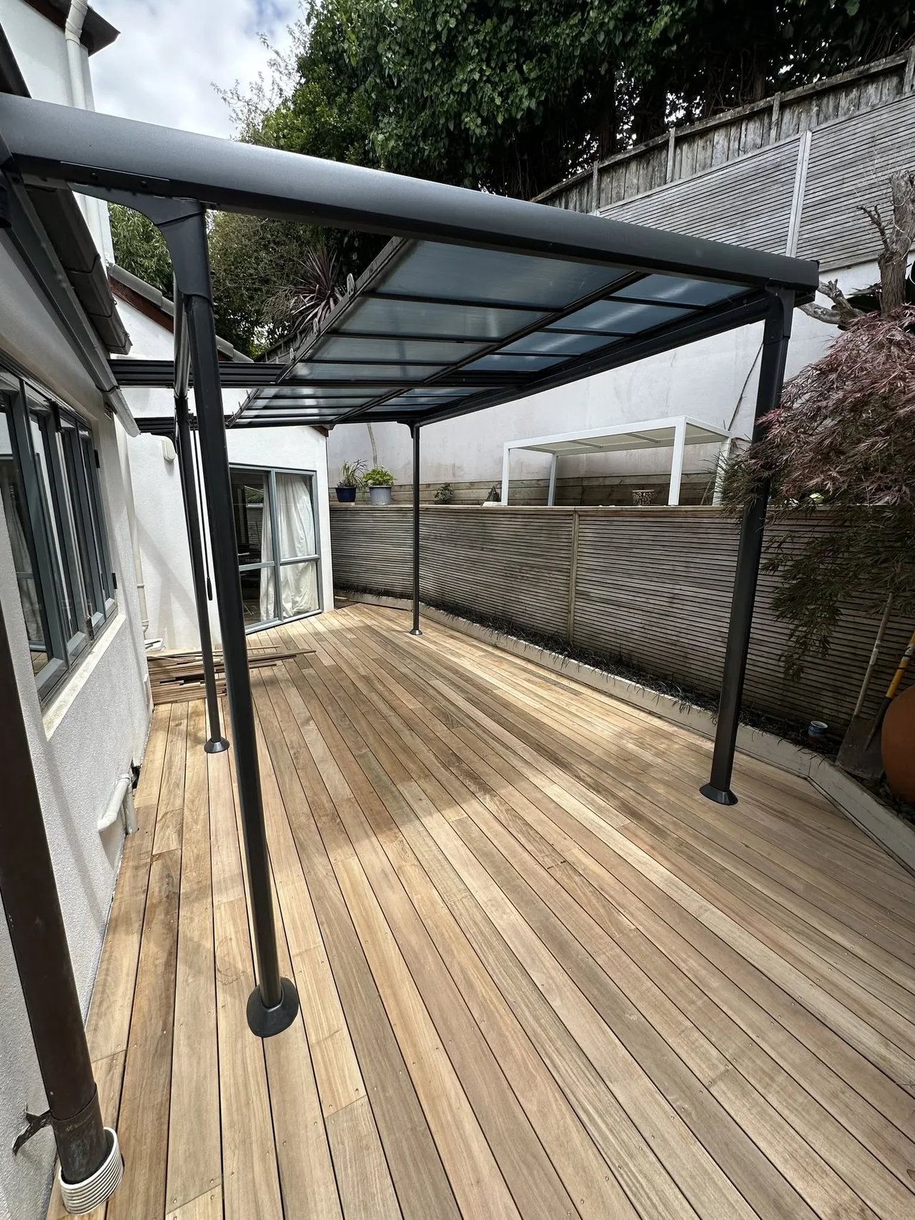 Covered pergola over timber decking alongside a home