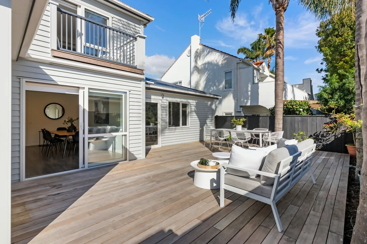 Finished deck with outdoor lounge furniture and open doors connecting to a white weatherboard home