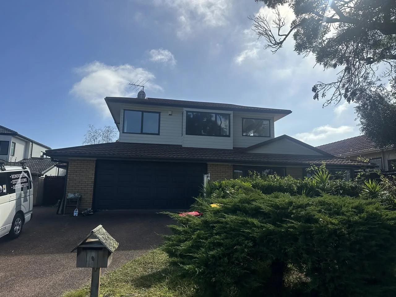 Two-storey home with refreshed white upper cladding, brick ground floor and dark garage doors